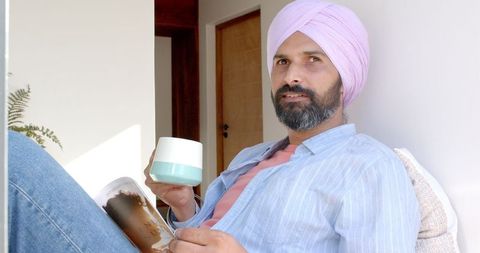 Man in turban relaxing at home with coffee and magazine