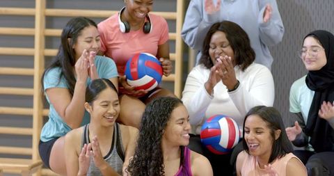 Multicultural female volleyball team celebrating together on bench in school gym