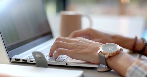 Man typing on slim white laptop with rose-gold watch in sunlit coworking workspace