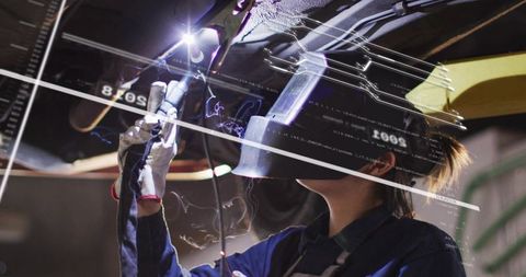 Automotive technician welding undercarriage with arc welder and protective helmet