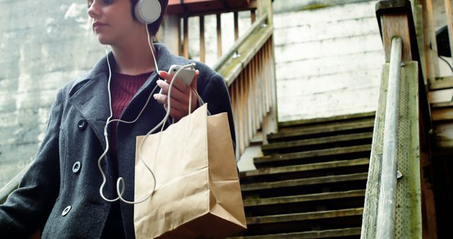 Young Woman Listening to Music While Carrying Shopping Bag on Urban Staircase - Download Free Stock Images Pikwizard.com