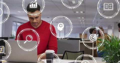 Young man in red sweater working on laptop with holographic UI overlay in modern office
