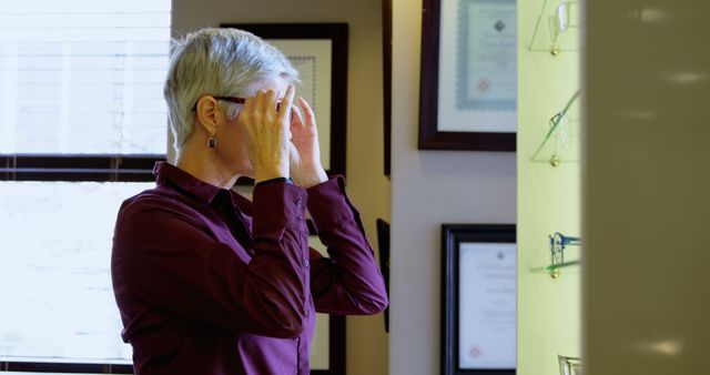 A senior Caucasian woman is trying on glasses at an optometrist's office, with copy space. She appears to be evaluating the fit and style of the eyewear as part of her vision care routine.