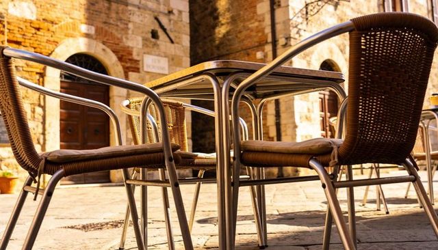 Sunlit wicker cafe chairs and table on historic stone plaza courtyard morning glow