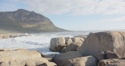 Waves Crashing on Rugged Coastline with Boulders and Mountain Views
