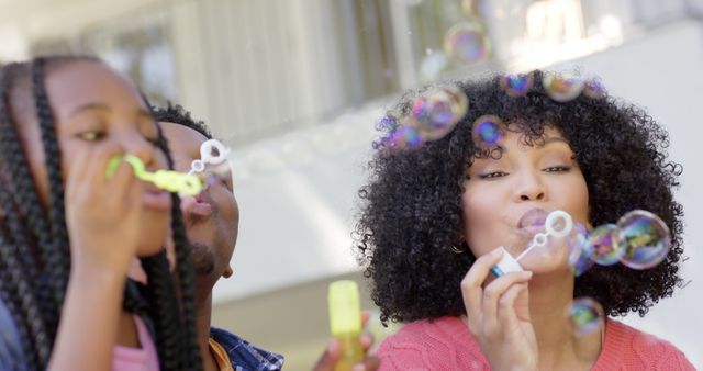 Happy african american parents with daughter blowing bubbles in garden at home. Domestic life, nature and lifestyle, unaltered.