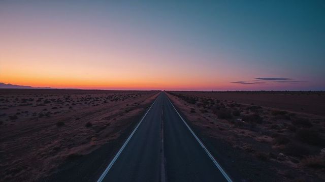Endless desert highway leading to distant horizon at sunset with colorful twilight sky