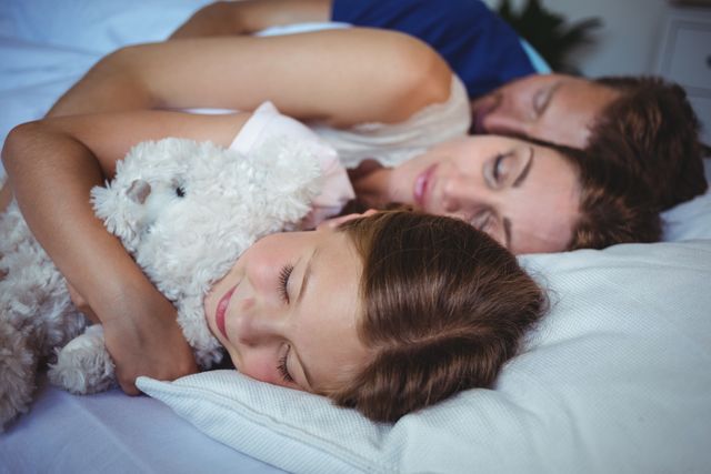 Family is sleeping closely together on a cozy bed at home, showing intimate and peaceful bonding moments. Ideal for use in ads related to family life, home comfort products, parenting articles, or sleep-related content.