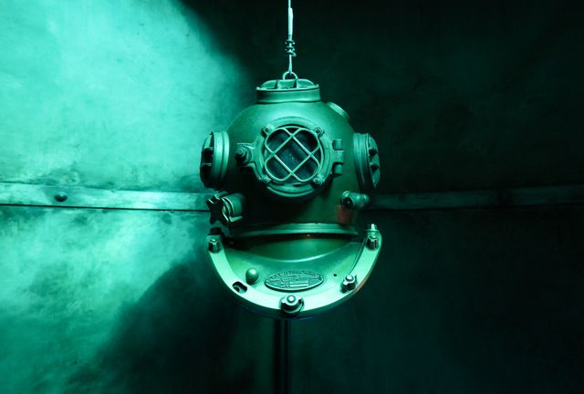 Vintage diving helmet illuminated by dramatic underwater lighting, showcasing intricate details. Perfect for use in maritime museum promotions, historical documentaries, underwater exploration themes, and vintage equipment articles.