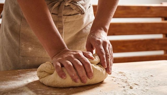 Rustic hands kneading dough on floured wooden countertop for artisan bread baking