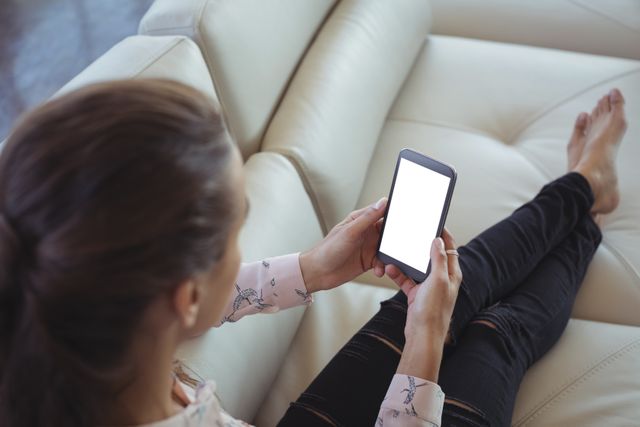 Businesswoman resting on a white sofa while holding a mobile phone. Ideal for illustrating concepts of work-life balance, modern office environments, and professional relaxation. Useful for business, technology, and lifestyle content.