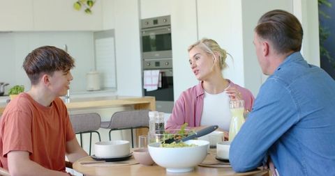 Family sharing casual breakfast at kitchen table, parents and teen son conversing