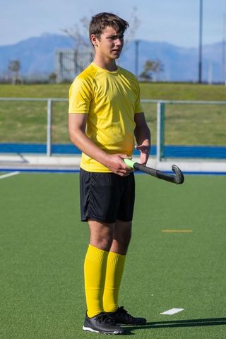 Teen Athlete Holding Hockey Stick on Field with Mountains in Background