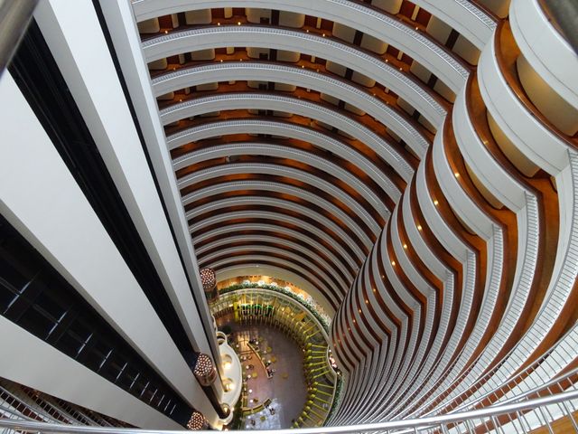 Elevated view of multi-story modern hotel atrium with curved balconies and well-designed interior. Suitable for use in travel-related materials, modern architecture promotions, hotel advertisements, hospitality industry marketing.