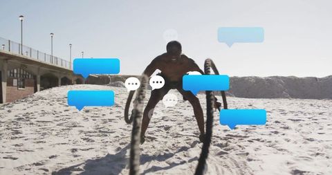Athletic Man Swinging Battle Ropes on Beach Surrounded by Social Media Icons