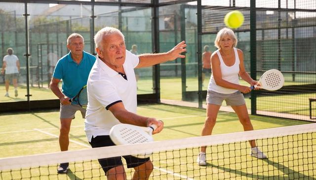 Senior players lunging and reaching while playing padel doubles on sunlit court