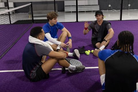 Tennis coach leading team huddle on purple indoor court during training session