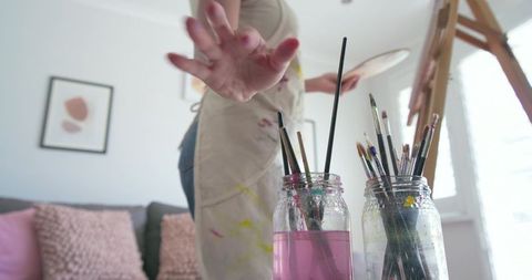 African American Painter Reaching for Brushes in Sunlit Home Studio with Easel