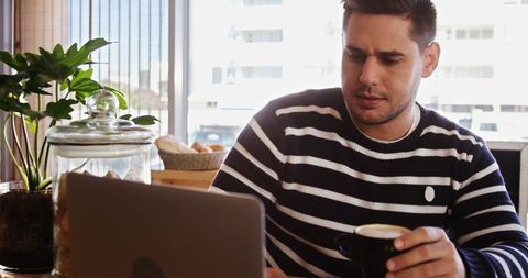 Man Studying Laptop in Coffee Shop While Holding Cup of Coffee