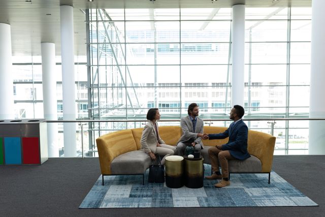 This image shows a diverse group of business professionals sitting and discussing in a modern office lobby. Ideal for use in corporate presentations, business websites, and articles about teamwork, diversity in the workplace, and professional collaboration.