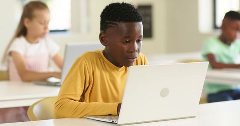 Focused African American Teen Boy Working on Laptop in Bright Classroom with Diverse Peers