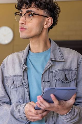 Young professional wearing tortoiseshell glasses holding tablet with blue-gray case in lounge