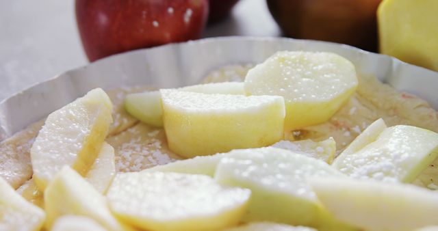 Close-up of an apple pie in preparation stage with fresh apple slices arranged on pastry dough. Suitable for illustrating home baking, holiday desserts, recipes, cooking blogs, and food preparation. It highlights the stages of making an apple pie and can be used in culinary articles, recipe books, and food-related advertisements.