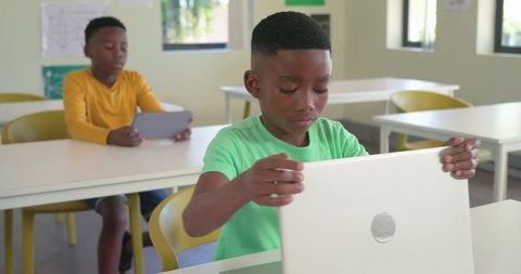 Focused African American Teen Boys Using Laptop and Tablet in Bright Modern Classroom