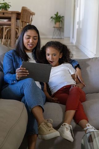 Mother and daughter watching tablet on sofa sharing surprised joyful family bonding moment