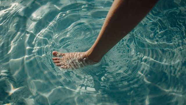 Bare foot dipping into turquoise pool creating sunlit ripples and water caustic patterns