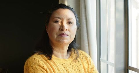 Mature Woman in Yellow Sweater Sitting By Window in Thoughtful Pose