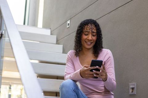 Smiling woman checks smartphone sitting on modern floating stairs