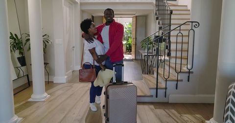 African american couple standing in modern entry holding luggage embracing happy return