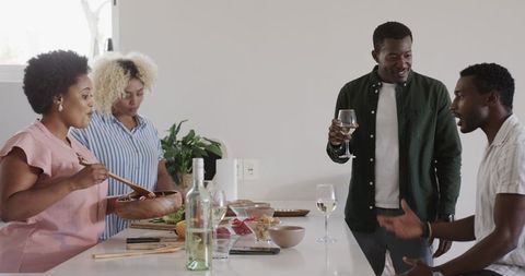 Black friends preparing dinner together tossing salad at modern kitchen island with wine