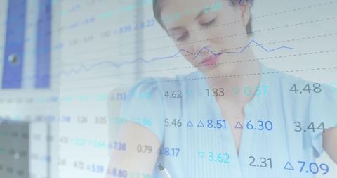 Business analyst writing notes while reviewing financial charts and dashboard data overlay