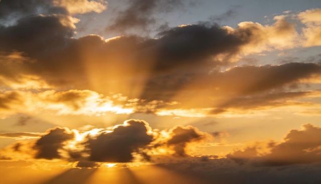 Golden sunrise rays breaking through cumulus clouds with dramatic crepuscular beams