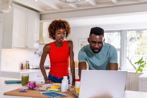 African american couple planning household finances at kitchen island leaning over laptop and paperw