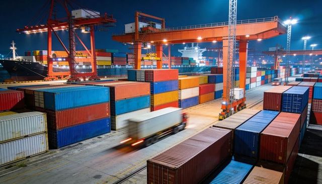 Nighttime container terminal with colorful stacked shipping containers and moving truck