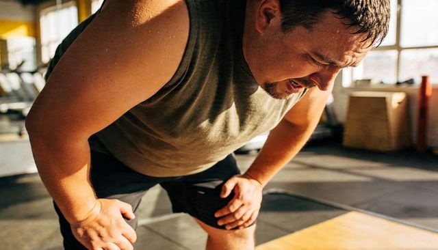 Man leaning forward sweating and catching breath after intense HIIT training in sunlit gym