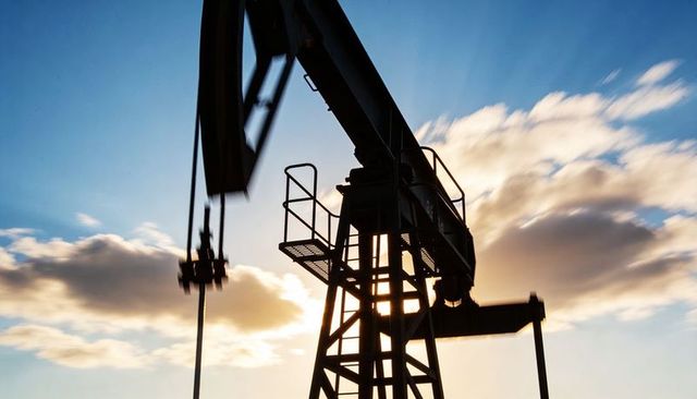 Sunset silhouette of pumpjack nodding donkey pumping rig over open oilfield horizon