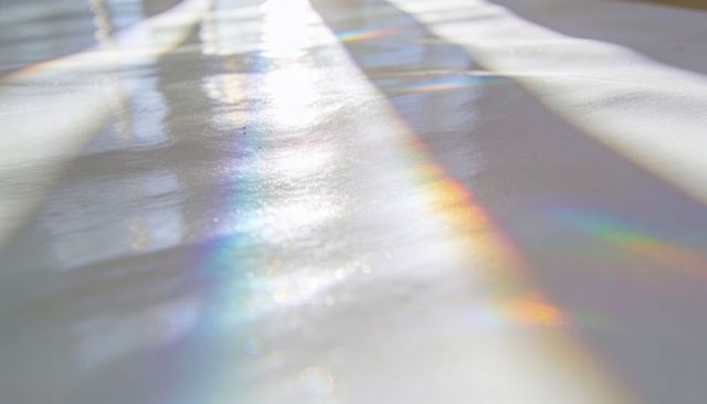 Prismatic sunlight casting rainbow bands across glossy sill with blind shadows