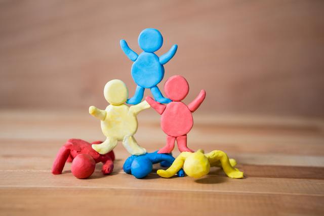 Colorful clay figurines forming a pyramid on a wooden surface, symbolizing teamwork and collaboration. Ideal for educational materials, children's art projects, creativity workshops, and playful learning environments.