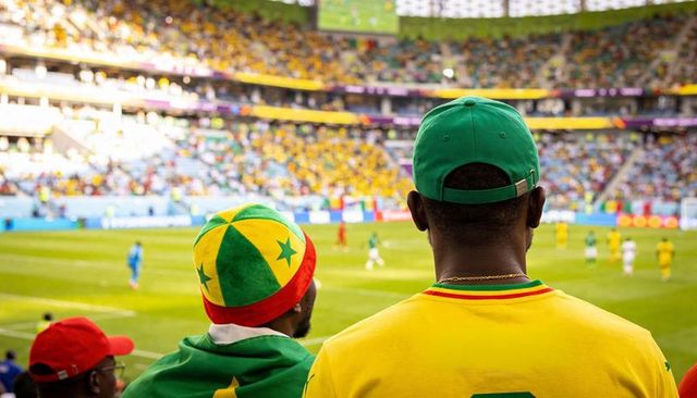 Cheering football fans wearing yellow jerseys with senegal star beanie in packed stadium
