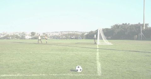 Youth soccer players walking toward goal with soccer ball in foreground on sunny field