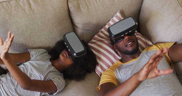 People lying on couch wearing VR headsets. Excellent for depicting modern technology, family entertainment, immersive experiences, and relaxation. Useful for articles on advancements in virtual reality, lifestyle blogs, and tech advertisements.