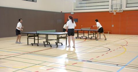 Friends playing doubles table tennis in gym