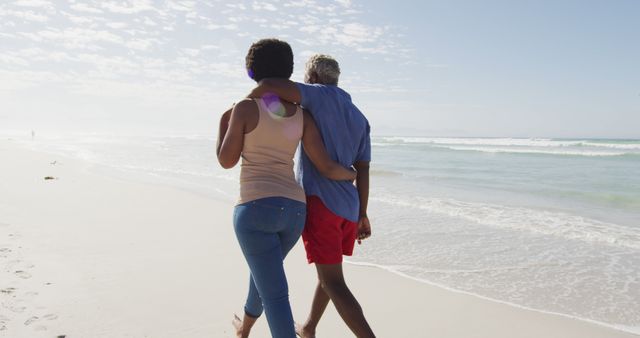 A couple walks along a beach, embracing under a sunny sky. The scene suggests a romantic, relaxing moment perfect for vacation or travel promotional materials, relationship articles, or lifestyle blogs. It captures themes of togetherness, love, and leisure.
