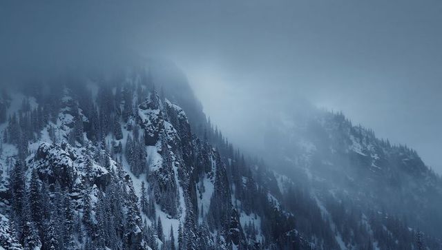 Fog-shrouding alpine ridge revealing steep snowy cliffs and conifer forest