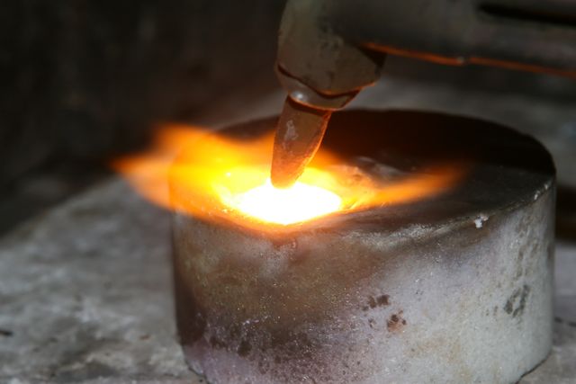 This close-up shows intense heat from a blowtorch melting metal. Suitable for content on metalworking, welding, craftsmanship, industrial processes, and showcasing labor-intensive skills in a workshop setting.