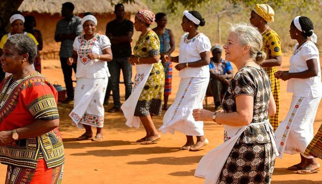 Senior traveler joining african village dance on red earth wearing white apron and dress